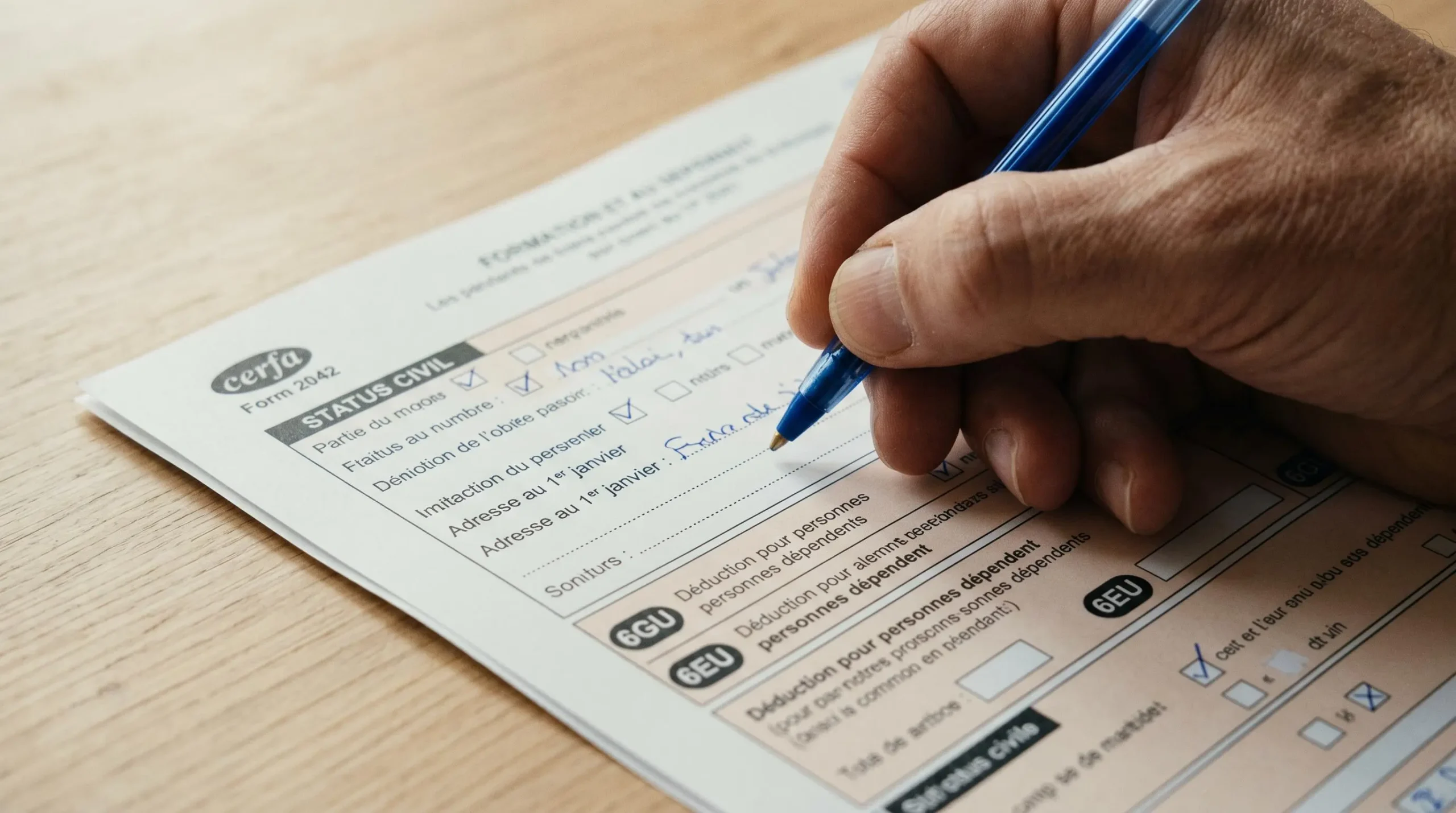 Main remplissant au stylo bleu un formulaire 2042 français, focus sur les champs d'adresse et les cases 6GU et 6EU de déduction